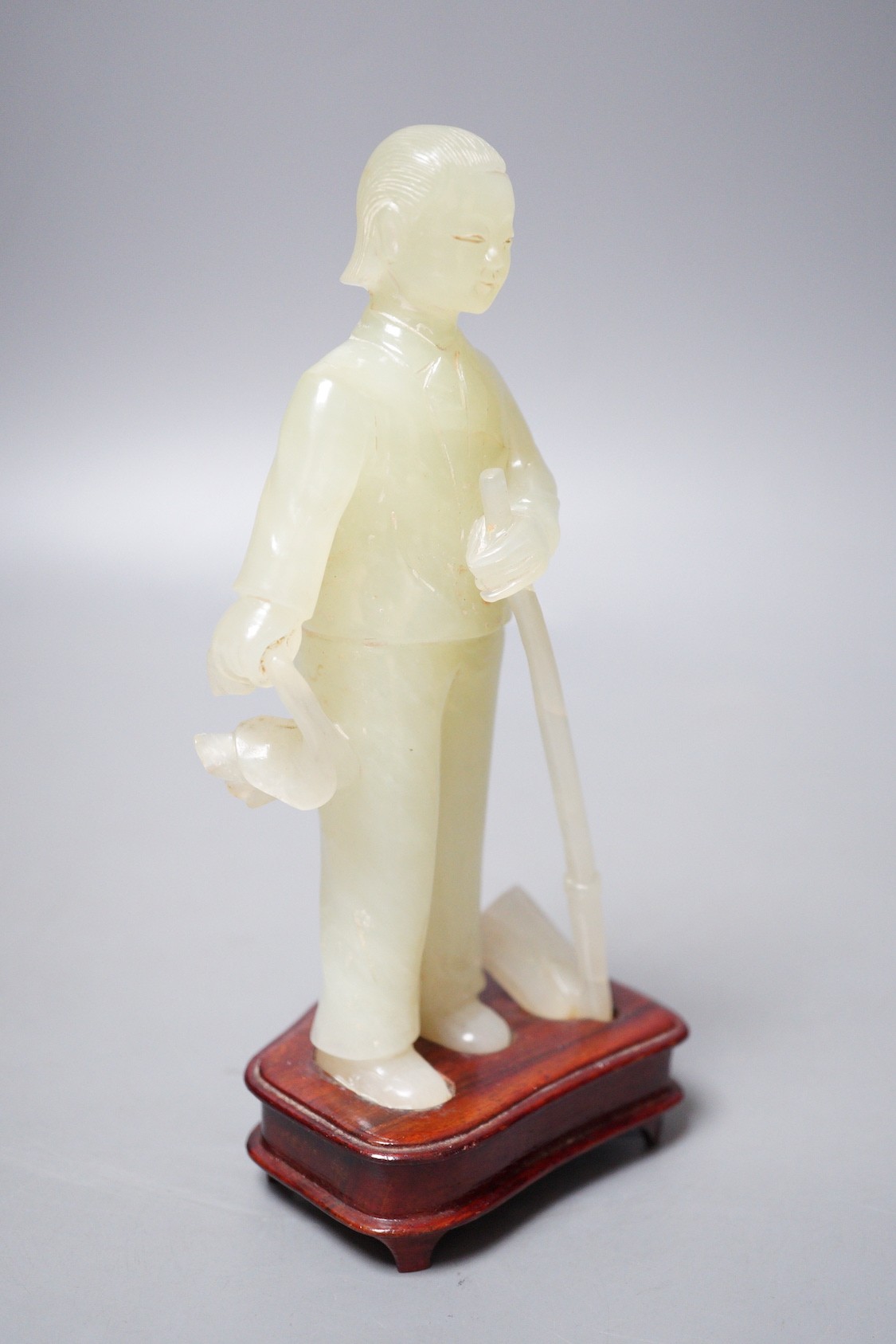 A Chinese carved bowenite jade figure of a worker on hardwood stand, 19cm